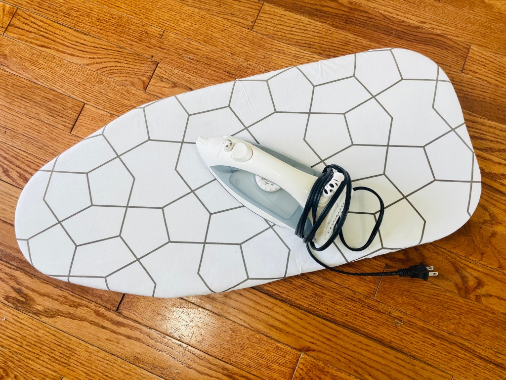 A blue and white iron sits on an ironing board with a black and white geometric design.